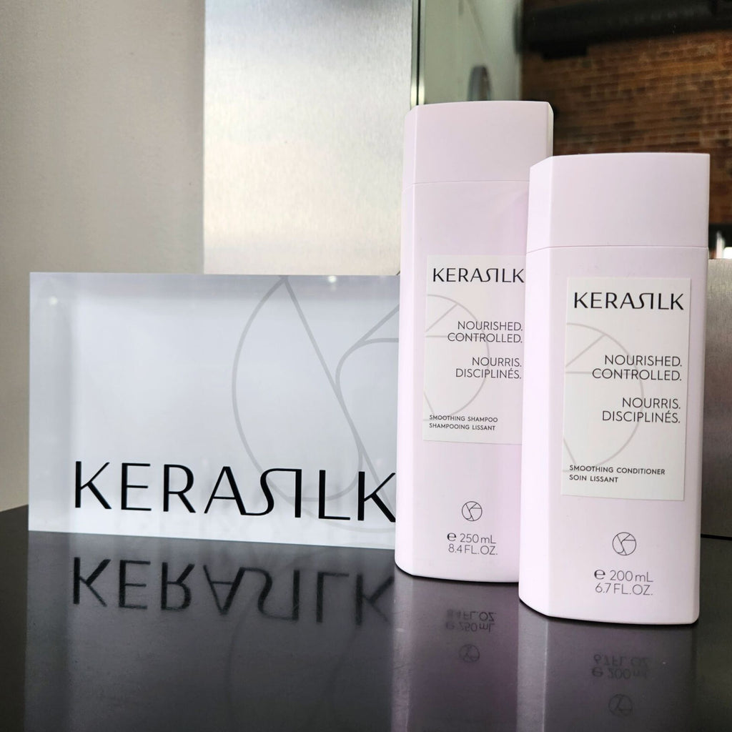 Two pastel pink Kerasilk bottles sitting next to a rectangle Kerasilk sign.