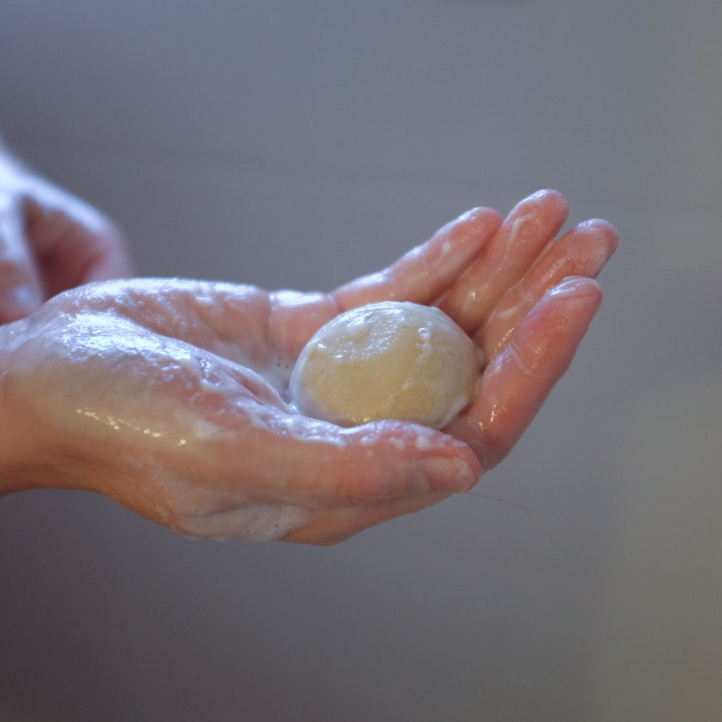 Hand holding hair cleansing bar in shower.