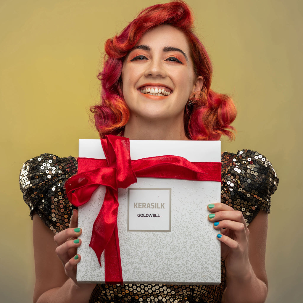 Red haired woman smiling holding red ribbon tied Christmas gift set